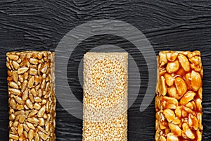 Cereal granola bar with peanuts, sesame and sunflower seeds on a cutting board on a dark stone table. View from above. Three