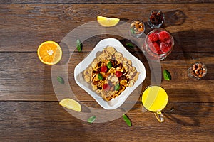 Cereal, morning breakfast, corn flakes, raisins, almonds, mint leaves, orange juice, strawberry, top view, on a dark wooden