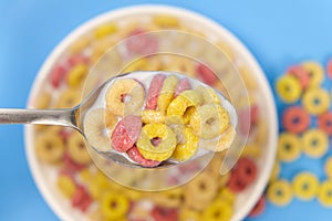 Cereal rings with milk, close-up in spoon, top view, blue background.