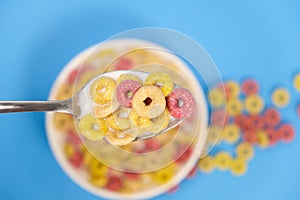 Cereal rings with milk, close-up in spoon, top view, blue background.