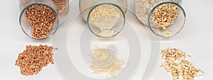 Cereals: buckwheat, rice, oatmeal spilled out of glass containers on a white table