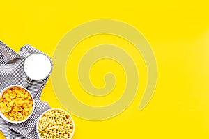 Cereals, oatflakes and cornflakes with milk and towel for healthy breakfast on yellow background top view mock up photo