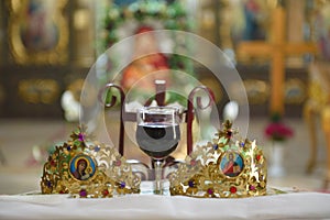 Ceremonial crowns and a glass of wine as orthodox wedding accessories.