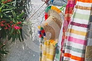 A ceremonial folk hat made of straw or plant fibers, decorated with colorful threads, hangs on a hook on a bench at a