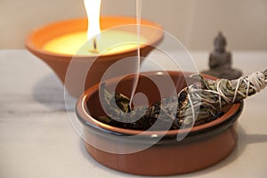 Ceremonial White Sage Smudge Stick burning with a candle flame burning in the background