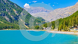 Ceresole Reale, Italy. View of Lake Ceresole on a sunny summer day. Some people windsurfing. Some houses of Borgata Borgiallo in