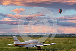 Cessna airplane in field at sunrise with hot air balloon in sky