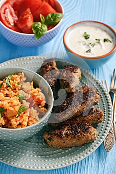 Cevapcici, balkanian grilled meat sausages with savory rice and yogurt dip.