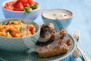 Cevapcici, balkanian grilled meat sausages with savory rice and yogurt dip.