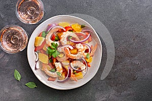 Ceviche with shrimps and orange, two glasses of pink sparkling wine, dark rustic background. Latin American food. Top view, copy