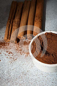 Ceylon cinnamon sticks and ground cinnamon bowl. Carelessly scattered cinnamon on the background