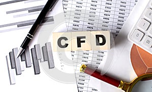 CFD text on wooden block on graph background with pen and magnifier