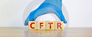 CFTR symbol. Wooden cubes with words `CFTR - cystic fibrosis transmembrane regulator`, doctor hand in blue glove. Beautiful whit photo