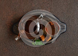 Chaga tea in a glass bowl and teapot on a brown background. Organic infusion with chaga mushrooms in a wooden tray. Top view, flat