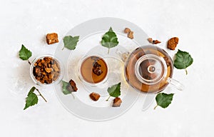 Chaga tea in glass bowls and teapot on a white background. Infusion with pieces of birch mushroom. View from above