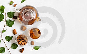 Chaga tea in a glass teapot and bowls, pieces of chaga mushroom, birch leaves on a white background. Copy space, top view