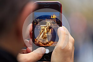 Chain Bridge in Budapest picture appears on tablet, smartphone in man`s hands. Blurred background