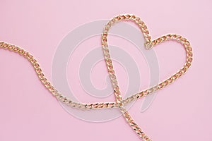 A gold chain laid out in the shape of a heart on a pink background