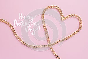 A gold chain laid out in the shape of a heart on a pink background