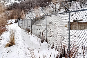 Chain link fence with barbed wires on snow covered hill slope viewed in winter