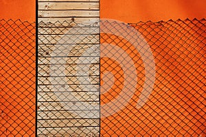 Chain link fence casting shadow over orange wall and doors shut with wooden planks