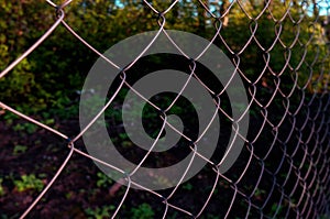 Chain-link fencing or Cyclone fence, hurricane fence, diamond mesh patterning. made from steel rods. another side is a green blurr