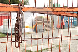 chain and pad key lock on orange locked gate for dirt yard parking lot. ph