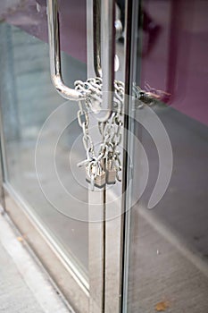 Chain and padlock on closed business glass door with metal handles