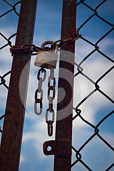 Chain and padlock hanging on an old gate with the blue sky in the background