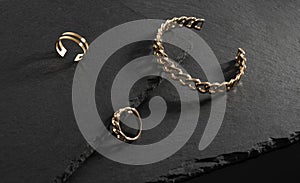 Chain shape golden bracelet and rings on black stone plates