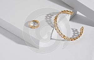 Chain shape golden modern bracelet and ring on white podium with copy space