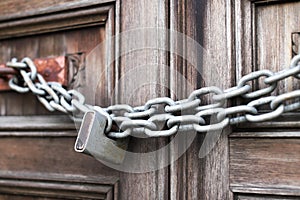A chain of silver color with closed padlock on an old gate. Closeup of old wooden door with closed padlock on a chain.