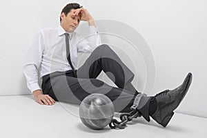 Chained businessman. Full length of depressed businessman sitting on the floor with shackles chained to his legs photo