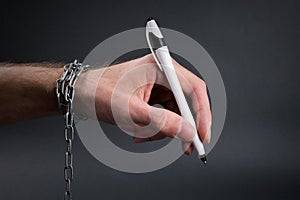 Chained hand holding  pen ready to sign
