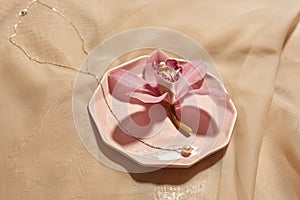 Chainlet and pink flower on plate on silk cloth