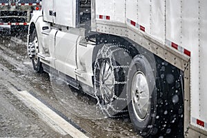 .Chains for better grip on slippery road surfaces on a white big rig semi truck drive axle wheel transporting cargo in dry van
