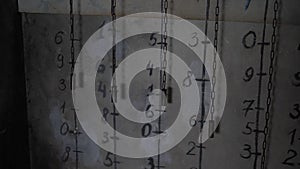 Chains hanging near a gray wall with various numbers in a dark scary room.