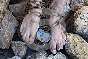 Chains with a lock on the legs of a slave amidst stones. Chains at the ankle. The symbol of slavery