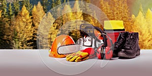 Chainsaw and protective equipment of lumberjack against forest background.