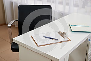 Chair and blank clipboard and pen on a table in office