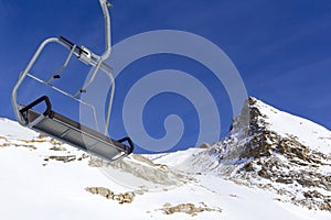 Chair lift in the foreground against the background of snow-capped mountains and blue sky.Austrian Alps in winter