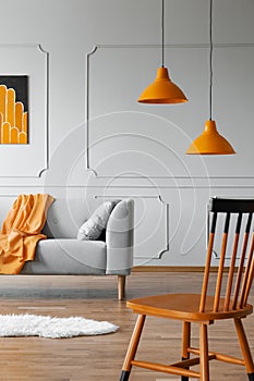 Chair in a living room interior with a wall molding, orange lamp and sofa. Real photo