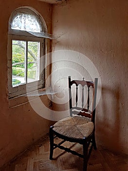 A chair next to a corner window with webs