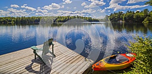 Chair sitting on a wood dock facing a calm lake with a red canoe