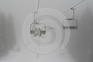 Chair ski lift with skiers silhouettes in deep mist