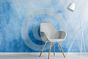 Chair and white lamp set on an empty, blue wall in living room i