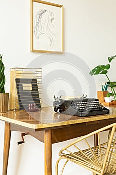 Chair at wooden desk with typewriter in classic workspace interior with poster on white wall. Real photo