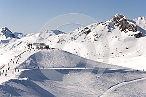 Chairlift station, skiers and ski piste in Alps