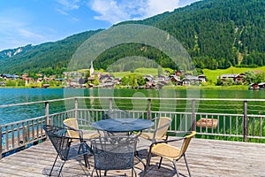 Chairs around table on terrace with view of Weissensee lake in summer time, Austria