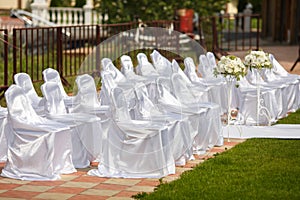 Chairs dressed in white satin wait for guests of a wedding